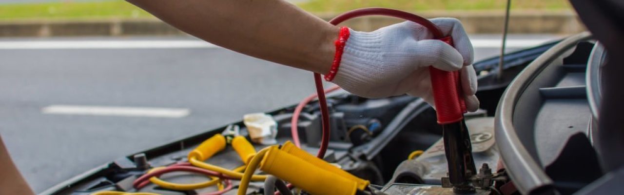 The technician uses a booster cable to connect the dead battery. Electric vehicle battery charging via jumper cable