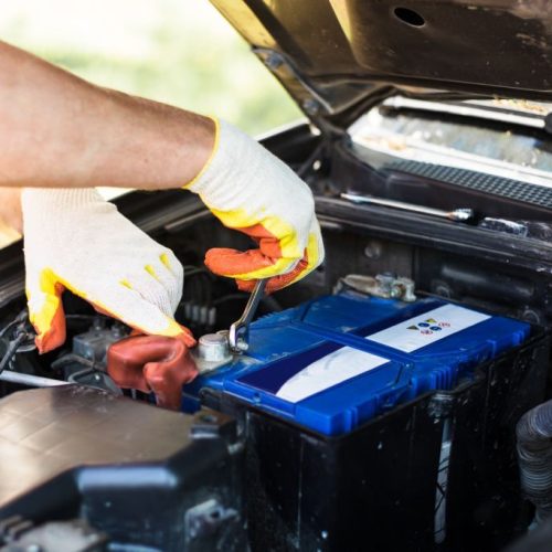 Replacing the battery in a car. The mechanic unscrews the battery fasteners with a screwdriver.